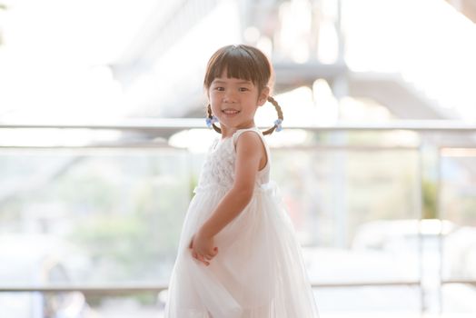 Happy cute little girl in white dress dancing. Asian family outdoor lifestyle with natural light.