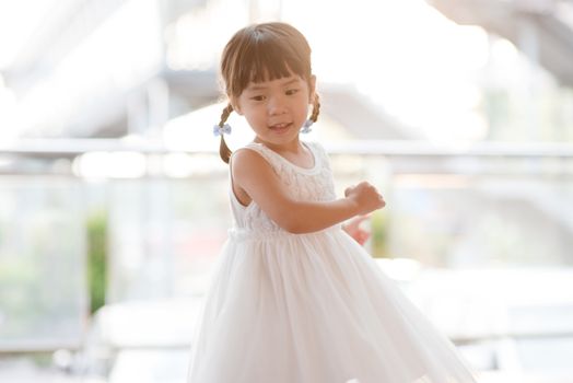 Happy little girl in white dress dancing. Asian family outdoor lifestyle with natural light.