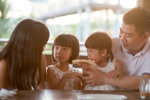 Happy children eating and sharing butter toast at cafe. Asian family outdoor lifestyle with natural light.