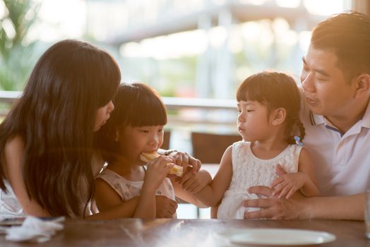 Children eating and sharing bread at cafeteria. Asian family outdoor lifestyle with natural light.