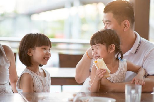 Happy children eating toast bread at cafeteria. Asian family outdoor lifestyle with natural light.