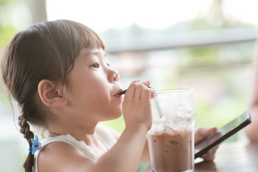 Little Asian girl drinking cold chocolate at cafe. Natural light outdoor lifestyle.
