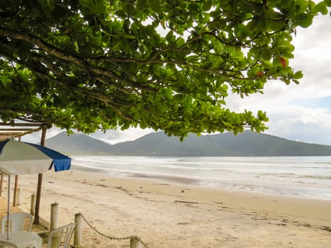 Sunny beach with waves in the background, green floats, chairs and umbrella in the foreground.