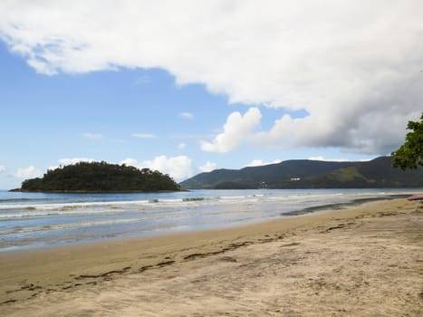 Beach landscape in Brazil, in sunny day with sand, waves and island in background and sky with clouds.