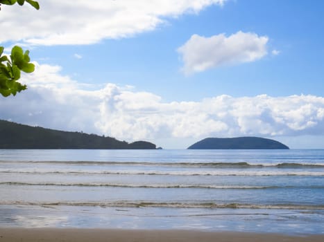 Beach in Brazil on sunny day and sea with waves, forest island in the background and clouds in the sky.