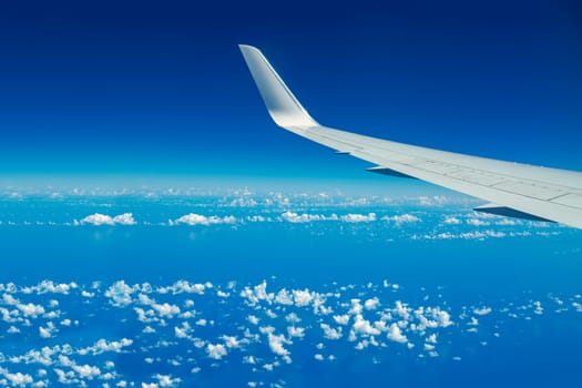 Looking through aircraft window during flight. Aircraft wing over blue skies and white clouds.Copy space.