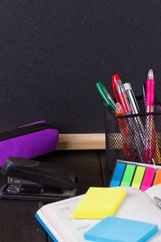 Pencil case with various stationery on old wooden table, on blackboard background