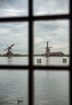 view from inside a mill to the authentic Zaandam mills on the water channel in Zaanstad village. Zaanse Schans Windmills and famous Netherlands canals, Europe.