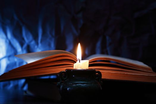 Still life with lighting candle near old book on dark blue background