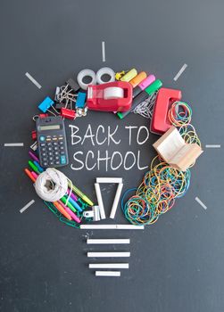 Back to school light bulb shape made with many pieces of stationery on top of a chalkboard 