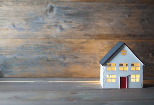 Model house with lights on inside over a wooden background