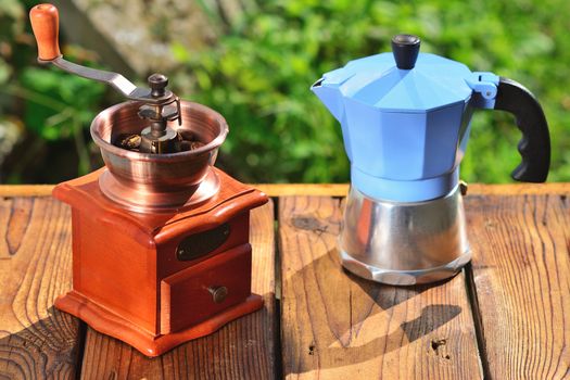 Coffee grinder and coffee maker on wooden boards on the background of green in the sunlight