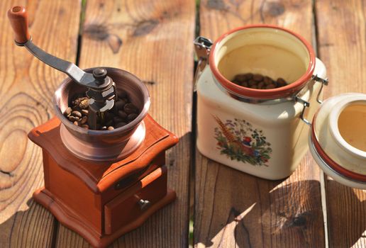 Coffee grinder with coffee beans and a jar with coffee beans on a wooden background