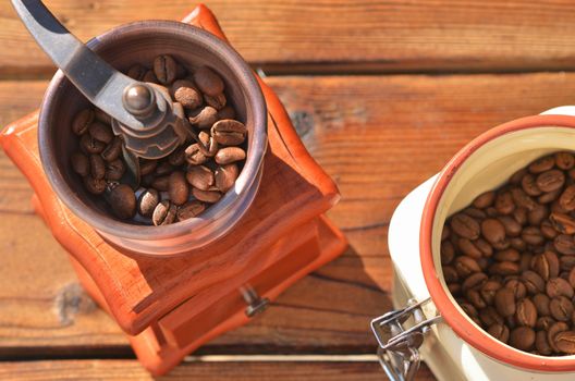 Manual coffee grinder and jar of coffee beans on wooden planks closeup