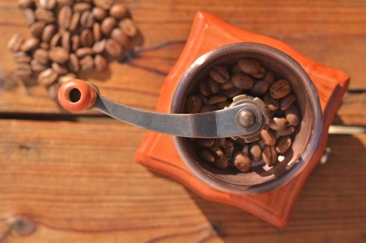 Manual coffee grinder with large coffee beans on wooden planks close-up, on a wooden background are grains