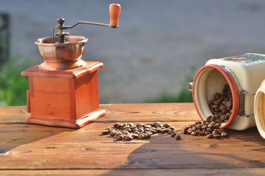 Frozen coffee beans are poured from the clay cans, there is a handmade coffee mill, against the background of greenery and water