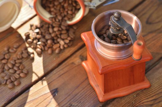 A clay jar from which poured grain and manual coffee grinder on wooden boards close up