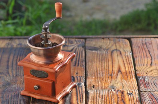 Manual horizontal coffee grinder with coffee beans on wooden boards against a background of green