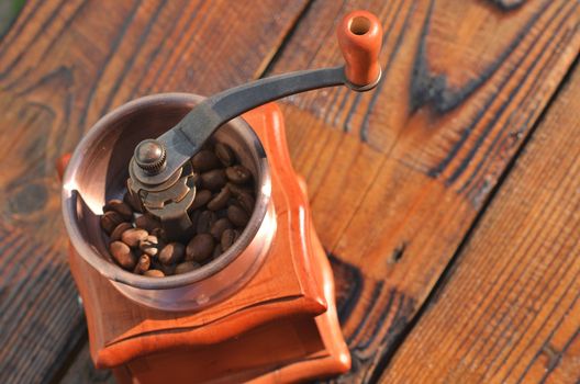 Manual horizontal coffee grinder with coffee beans on wooden boards, is in the lower left corner, close-up