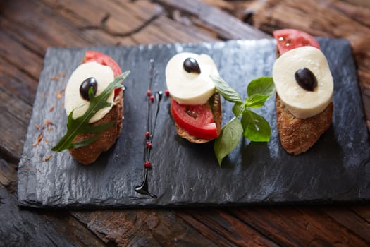 Italian bruschetta with chopped tomatoes, basil, mozzarella cheese and balsamic vinegar. Fresh homemade caprese bruschetta or crostini over black stone background, copy space.