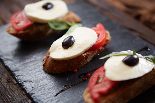 Italian bruschetta with chopped tomatoes, basil, mozzarella cheese and balsamic vinegar. Fresh homemade caprese bruschetta or crostini over black stone background, copy space.
