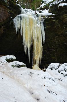 Frozen waterfalls on the rock, orange colored and snow