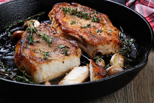 Fried pork steak in oil with herbs and garlic  in a cut in the frying pan. Close-up.