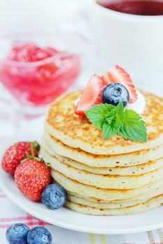A stack of pancakes decorated with ripe raspberries, blueberries and sour cream close-up
