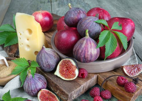 Ripe figs, red raspberry and apples, cane sugar and cheese are on old cutting board as well as green leaves lie on the old wooden table