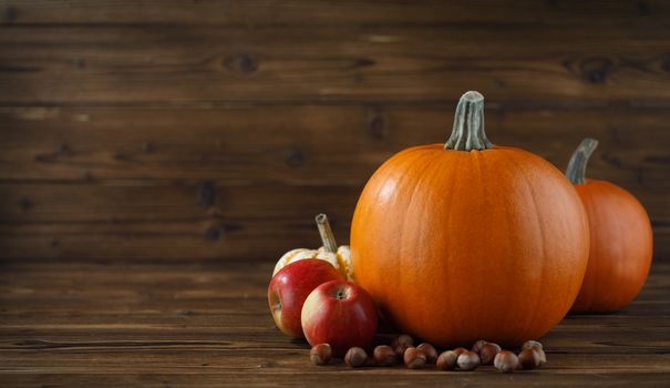 Autumn harvest still life with pumpkins, apples and hazelnuts on wooden background