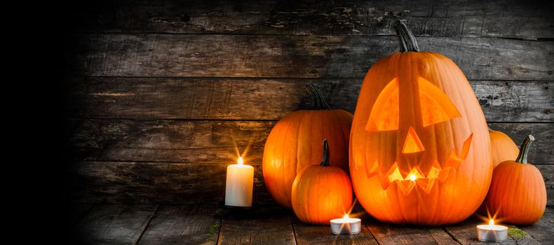 Halloween pumpkin head jack o lantern and candles on wooden background