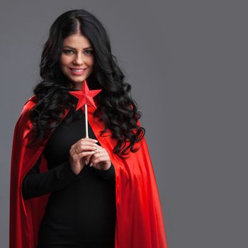 Woman in red cape with star shaped magic wand, gray background