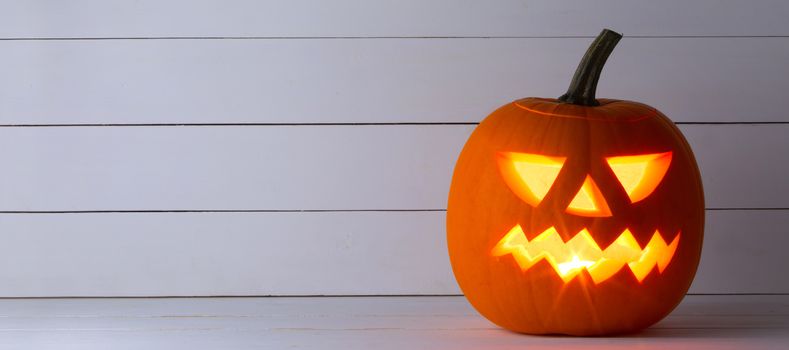 Glowing Halloween pumpkin head jack lantern on white wooden background