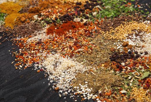 Different herbs and spices on black wooden background. Closeup. Colorful food background