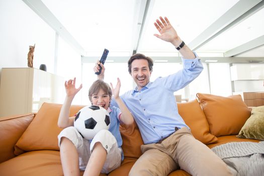 Portrait of happy boy watching soccer match with father on sofa at home