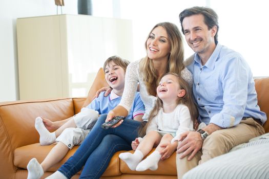 Adorable family with two children watching tv in the living room and smiling