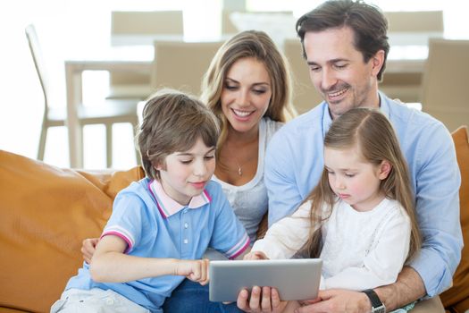 Portrait of happy family with two children sitting on sofa and using digital tablet pc