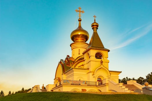 Beautiful view during sunset at the temple of St. Seraphim of Sarov in the city of Khabarovsk. A beautiful green lawn in the foreground. Religious architecture, buildings and traditions. Russia.