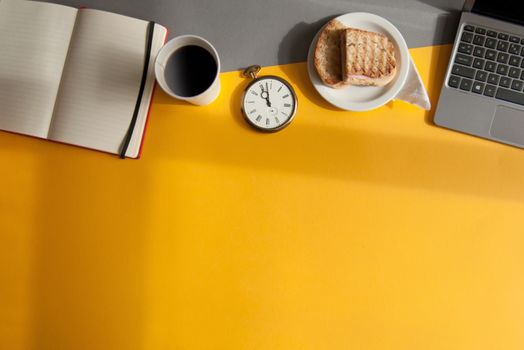 Business accessories including laptop, clock with grilled sandwich view from above