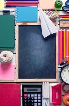 Top view of various stationery objects with blackboard in the centre and paper plane