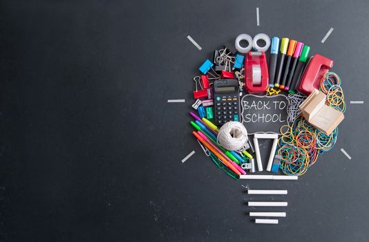 Light bulb shape made with many pieces of stationery on top of a chalkboard with space in the middle