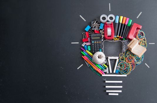 Light bulb shape made with many pieces of stationery on top of a chalkboard with space in the middle