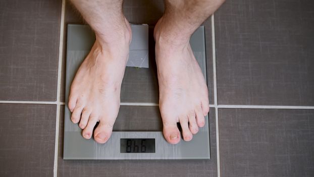 Male feet on glass scales, men's diet, body weight, close up, man standing on scales, top down view