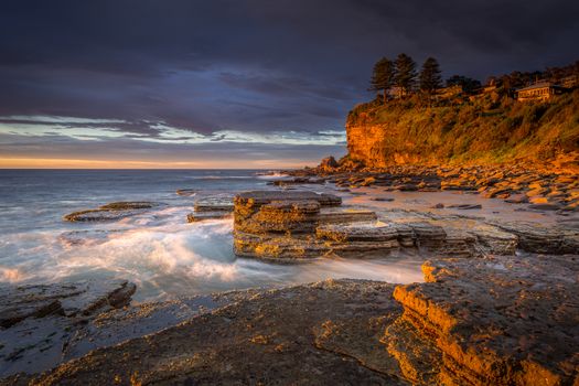 First light at Avalon beach, rich golden orange tones of light striking the cliff faces and rocks