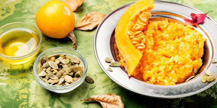 Homemade tasty porridge with orange pumpkin on green background