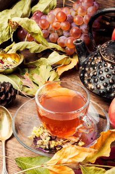 Cup with tea on an autumn background of fallen leaves, apples and grapes.Autumn postcard