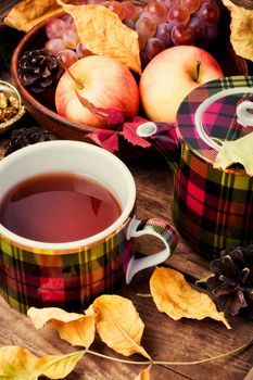 Cup with tea on an autumn background of fallen leaves, apples and grapes.Autumn still life