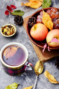 Cup with tea on an autumn background of fallen leaves, apples and grapes.Autumn postcard