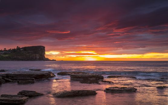 Coastal sunrise with blazing red skies filling the entire sky and casting reflected light onto the ocean 