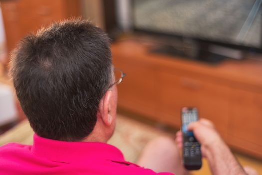 Back view of senior man watching tv holding remote control